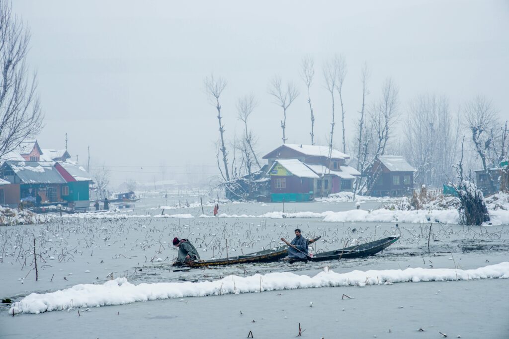 Two individuals paddle through snowy landscapes in Kashmir, showcasing the serene winter beauty.