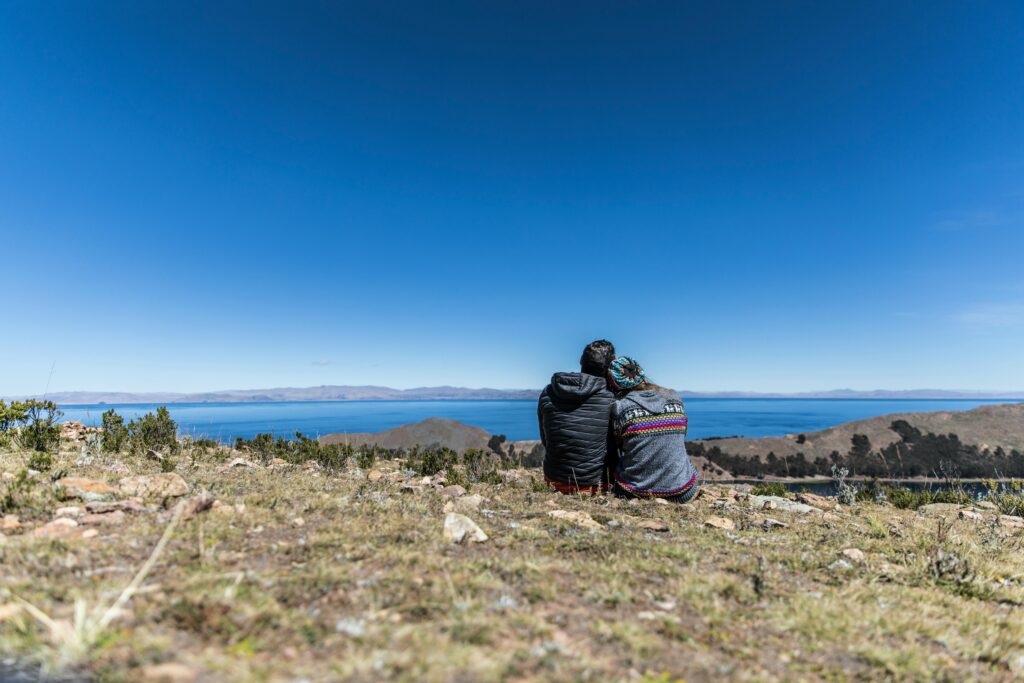 A couple sits on a mountain top, overlooking Lake Titicaca in Bolivia, enjoying a sunny day.