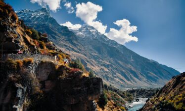 Scenic view of majestic mountains and stream in Kedarnath, India, under a clear blue sky.