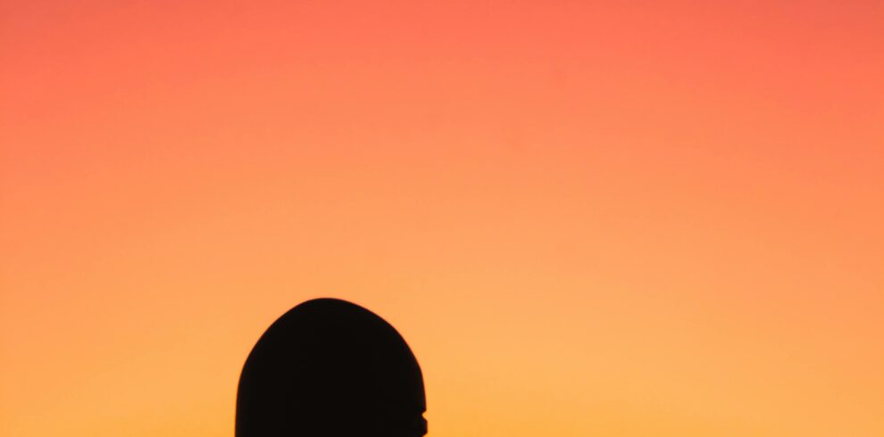 Silhouette of a Shiva Lingam against an orange and pink sunset sky in India.
