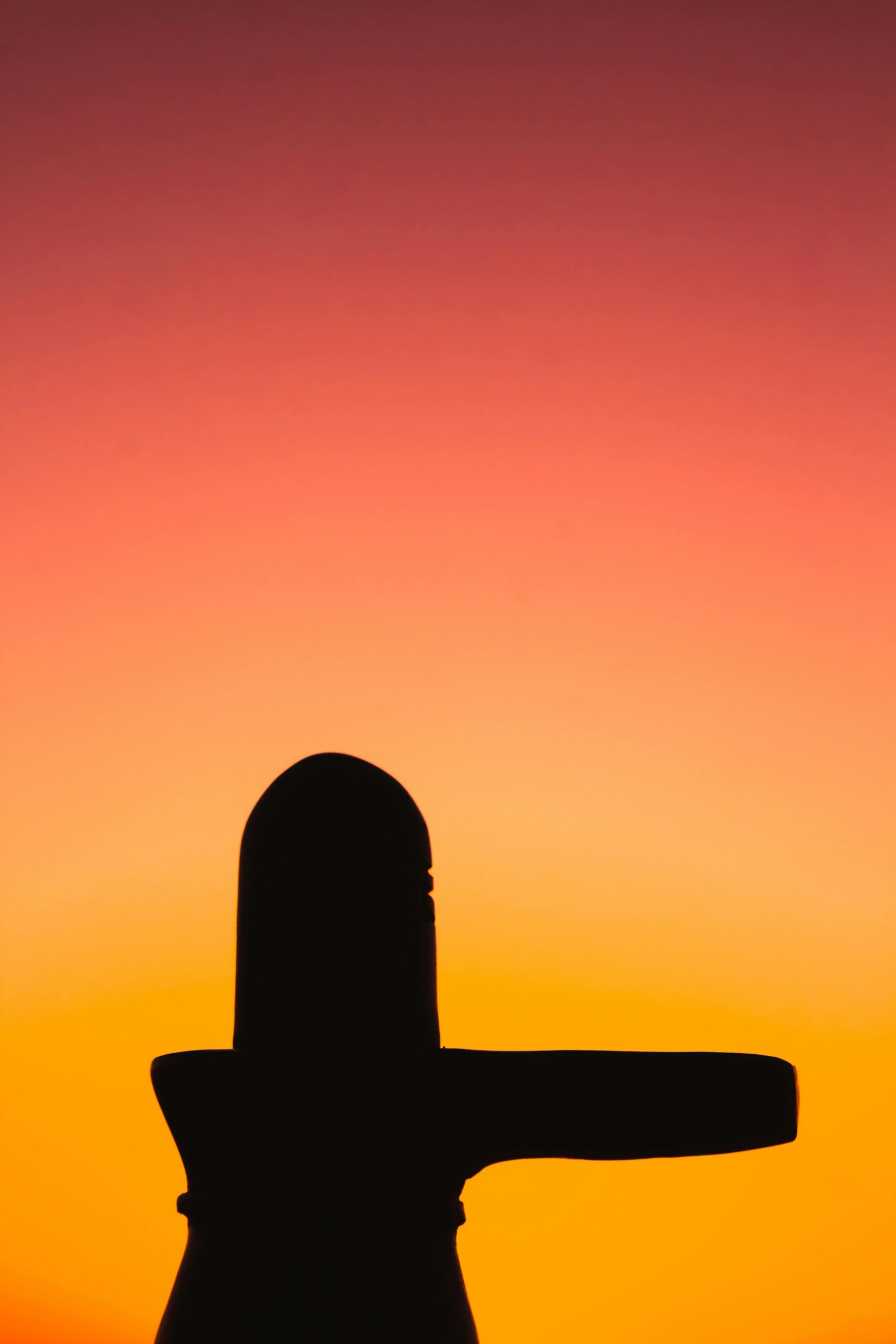 Silhouette of a Shiva Lingam against an orange and pink sunset sky in India.