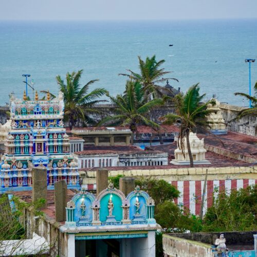 Vibrant Indian temple near the ocean, surrounded by palm trees and bright architecture.