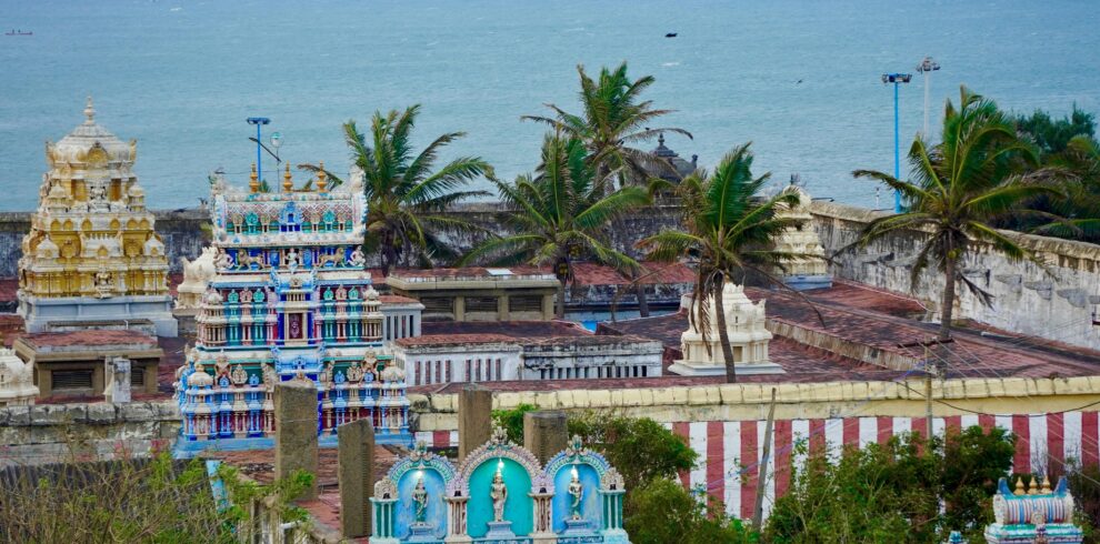 Vibrant Indian temple near the ocean, surrounded by palm trees and bright architecture.