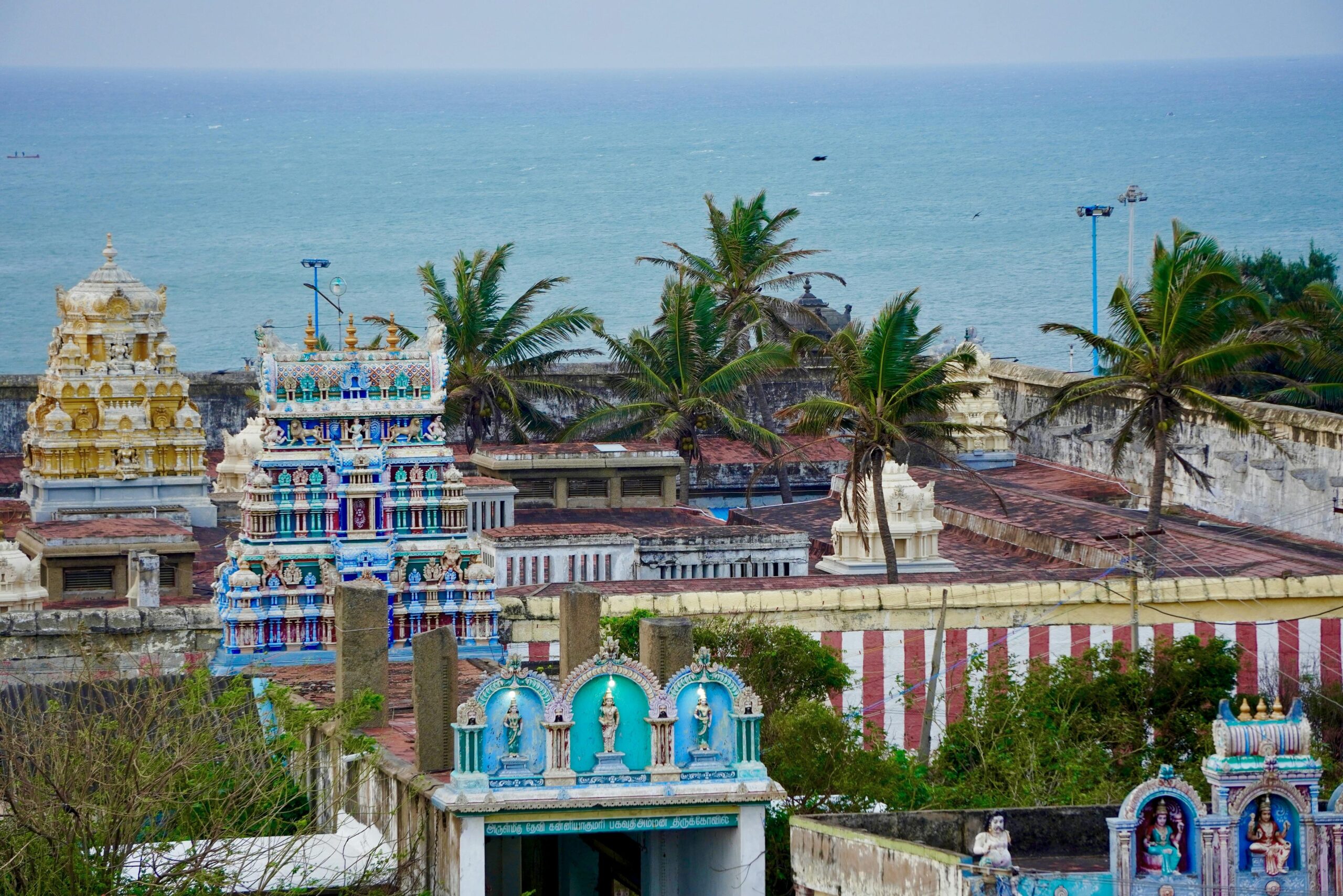 Vibrant Indian temple near the ocean, surrounded by palm trees and bright architecture.